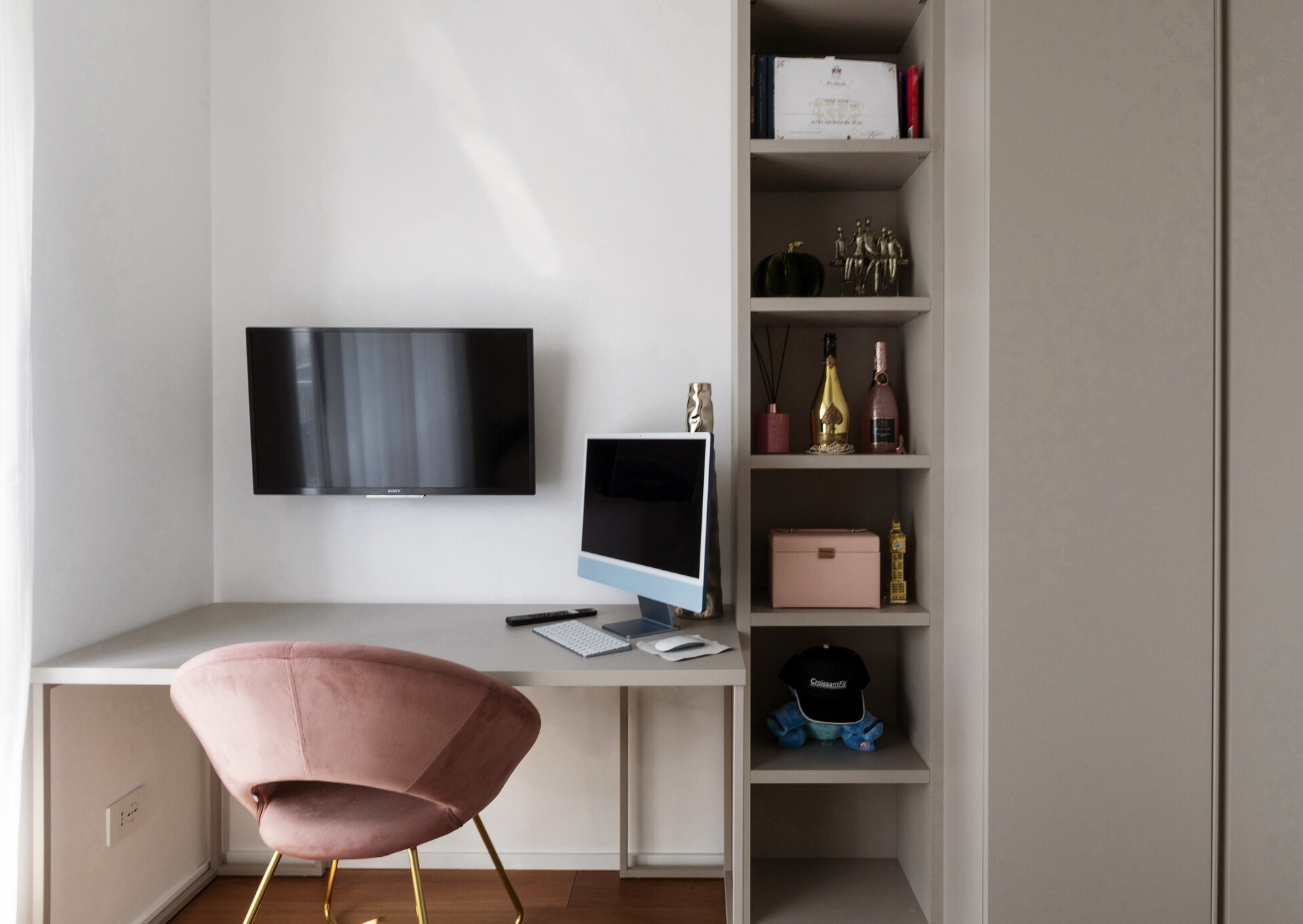 A compact guest bedroom features a single bed with built-in storage, overhead cabinets, a dedicated desk, open shelving, and a pink upholstered chair.